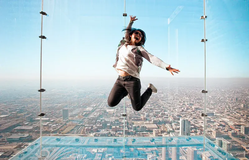 Visitor jumping on The Ledge glass-floor balcony at Skydeck Chicago, downtown grid below